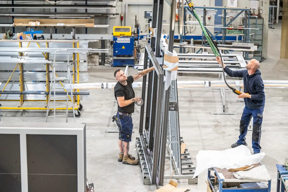Mitarbeiter montieren ein großes Fassaden-Element in der Werkstatt im Metallbau